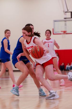 Player drives forward with the basketball while teammates and opponents move in the background.