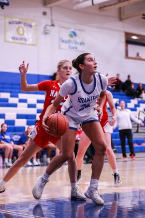 Players from opposing teams dive for loose basketball on gymnasium floor during competitive game.