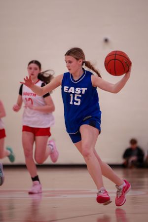 Player in blue East jersey number 15 dribbles the basketball down the court.