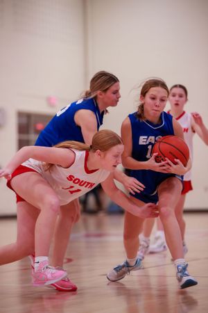 Players from East and South teams scramble for possession of the basketball during an intense play.