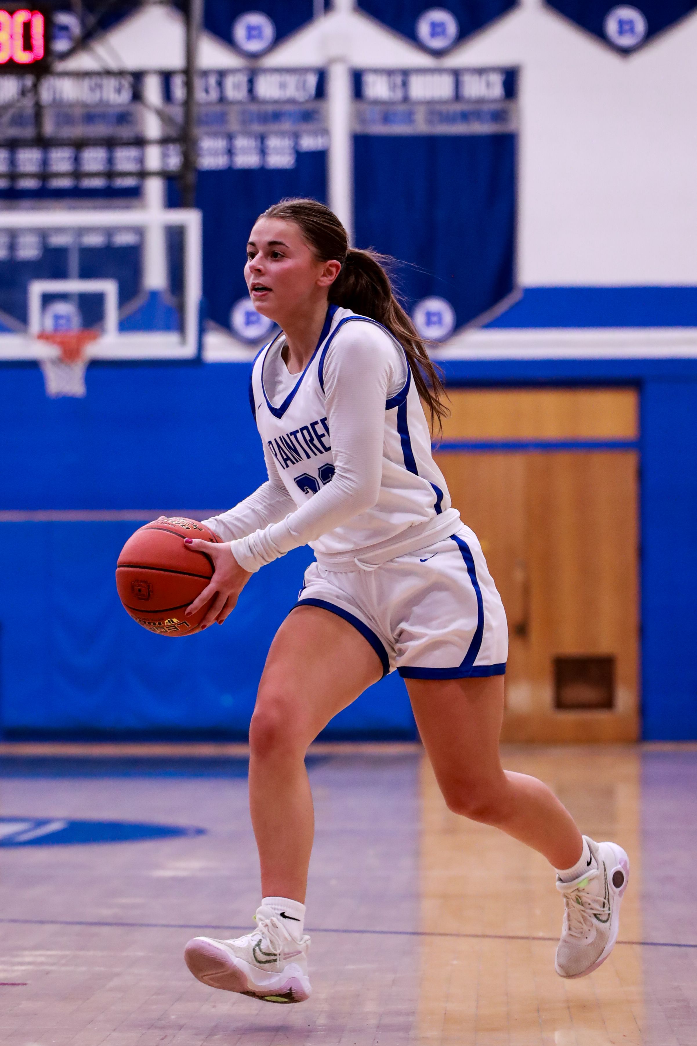 Basketball player in white uniform dribbles low while making offensive move on court.