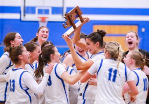 High school basketball team celebrates with championship trophy in blue and white gym.
