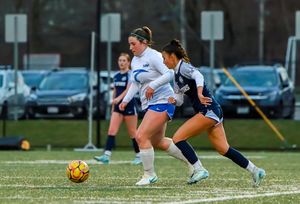 Athletes practicing soccer moves on a sports field with parked cars in background.