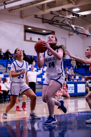 Basketball players in white uniforms practice defensive drills on gymnasium floor.