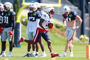 Football players in practice uniforms gather on the sidelines during training.