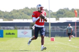 Football player practices throwing mechanics on practice field with equipment visible.