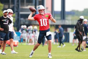 Football quarterback in red jersey practices throwing during team training.