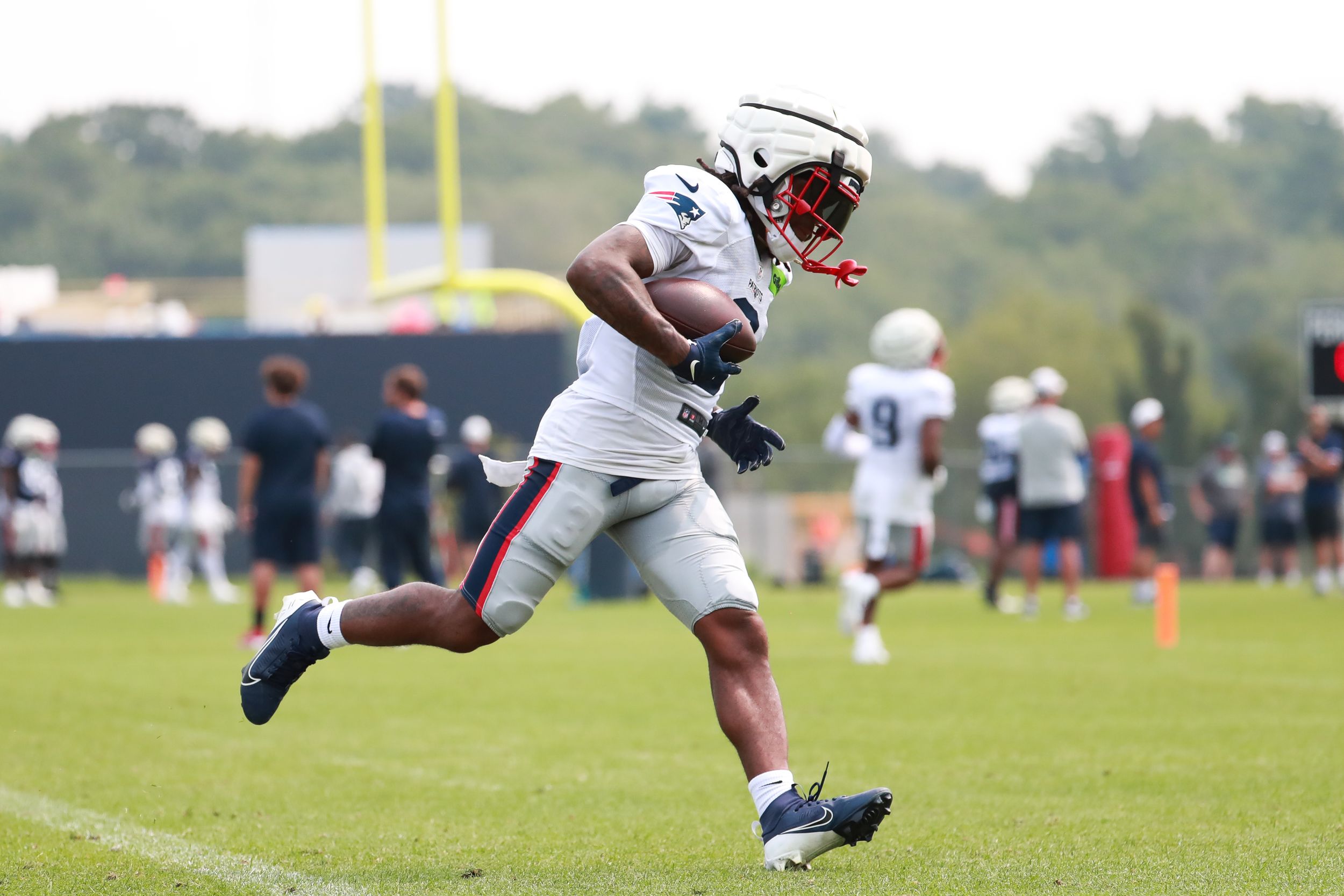Football player in white uniform runs with the ball during practice drills.