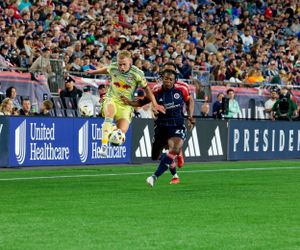 Soccer players compete in front of a packed stadium with advertising boards visible.