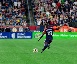 Soccer action unfolds on a green pitch with stadium advertising boards in view.