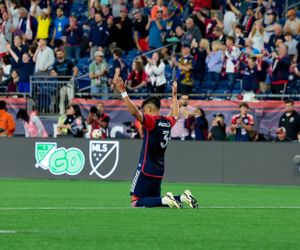 Players compete for the ball during a professional soccer match with a crowd in the background.