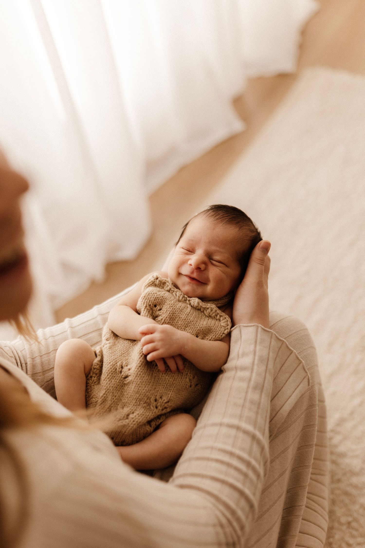 Sleeping newborn baby smiling while being cradled in warm natural light.
