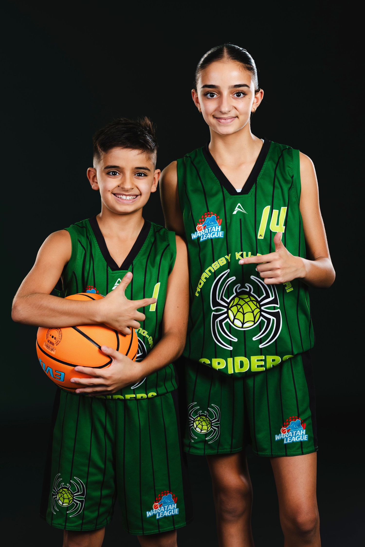 Two basketball players in green Spider uniforms pose with a basketball against a dark background.