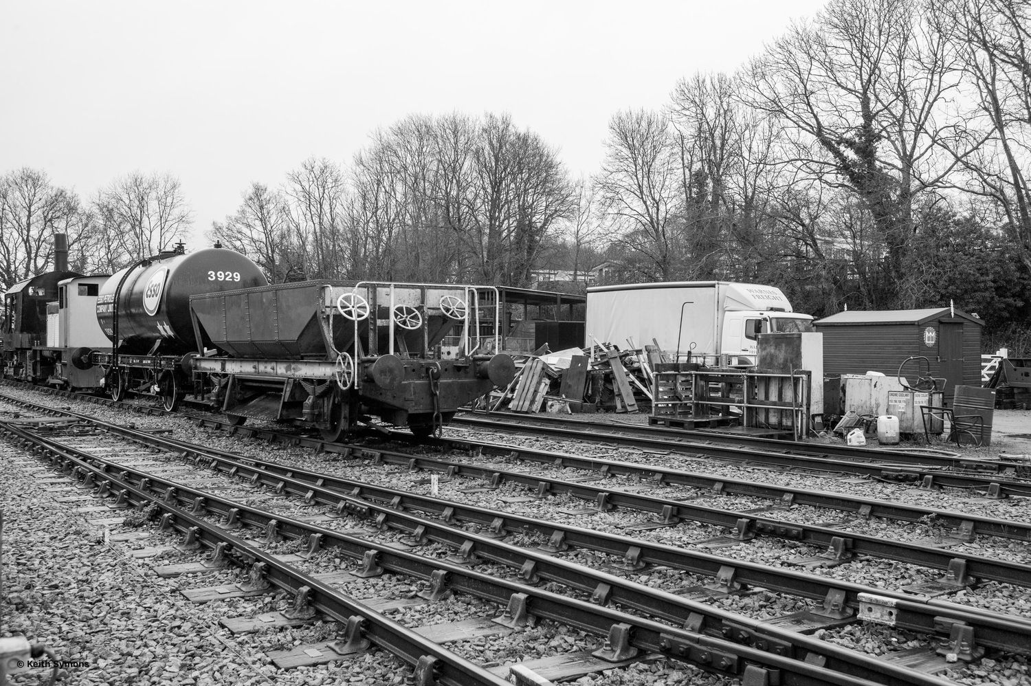 Black and white photograph of a vintage railway yard with multiple tracks and maintenance equipment visible.