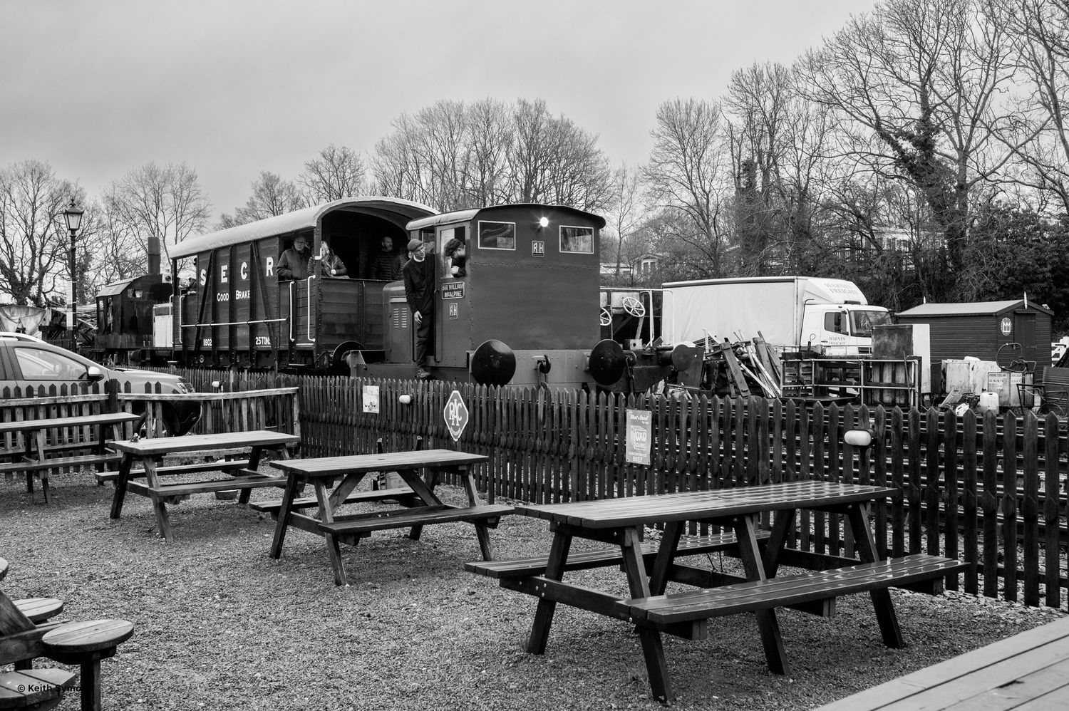 Black and white panoramic view of outdoor picnic tables and benches in a park setting during winter.