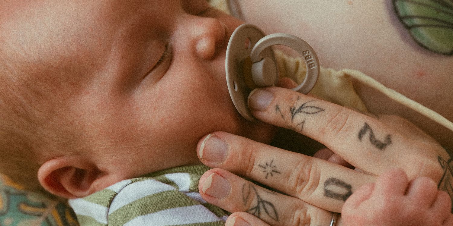 Close-up of a newborn baby nursing while mother's tattooed hand gently supports the infant's head.