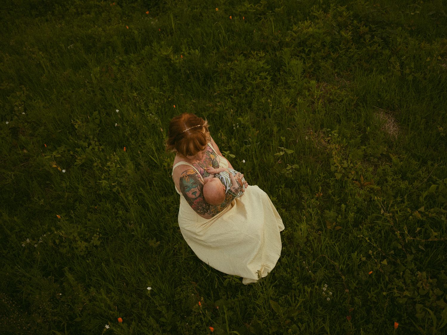 Aerial view of a tattooed woman in a white dress standing on lush green grass, shot from above.