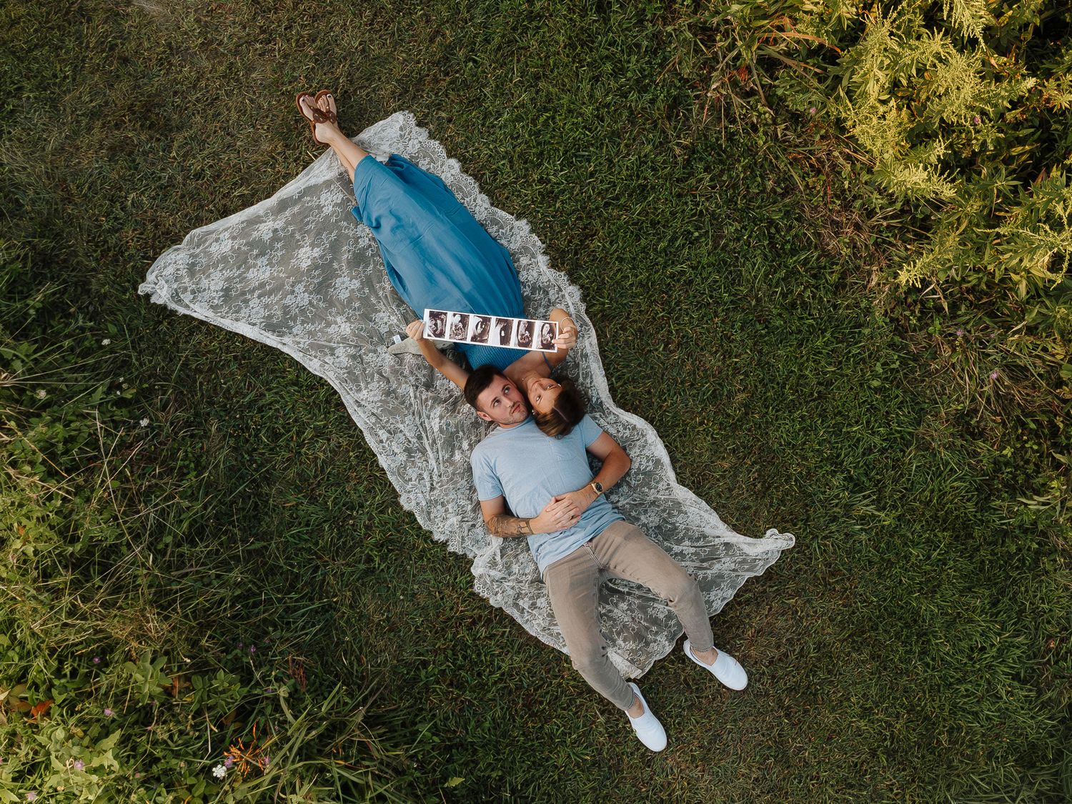 Aerial view of person lying on white blanket in green grass.