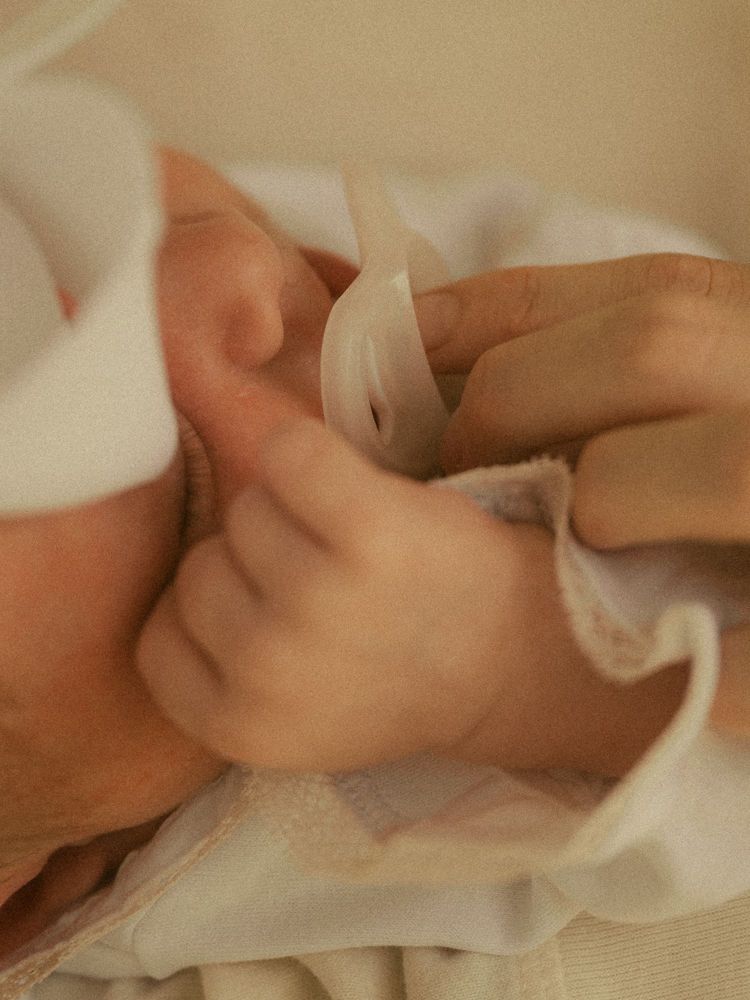 Newborn baby wrapped in a soft white blanket and hat, with an adult hand gently holding them close.