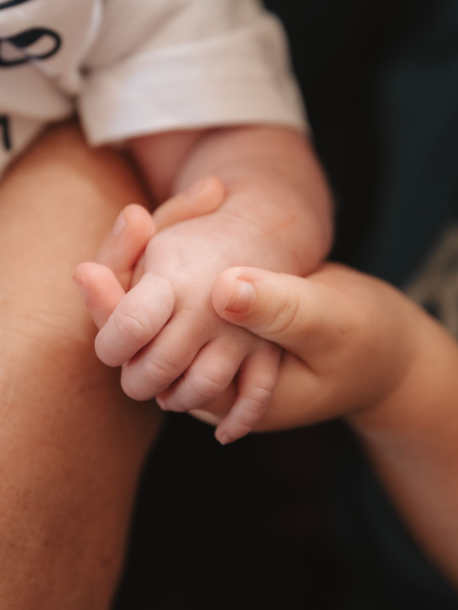 Close-up of tiny baby fingers grasping an adult's hand.