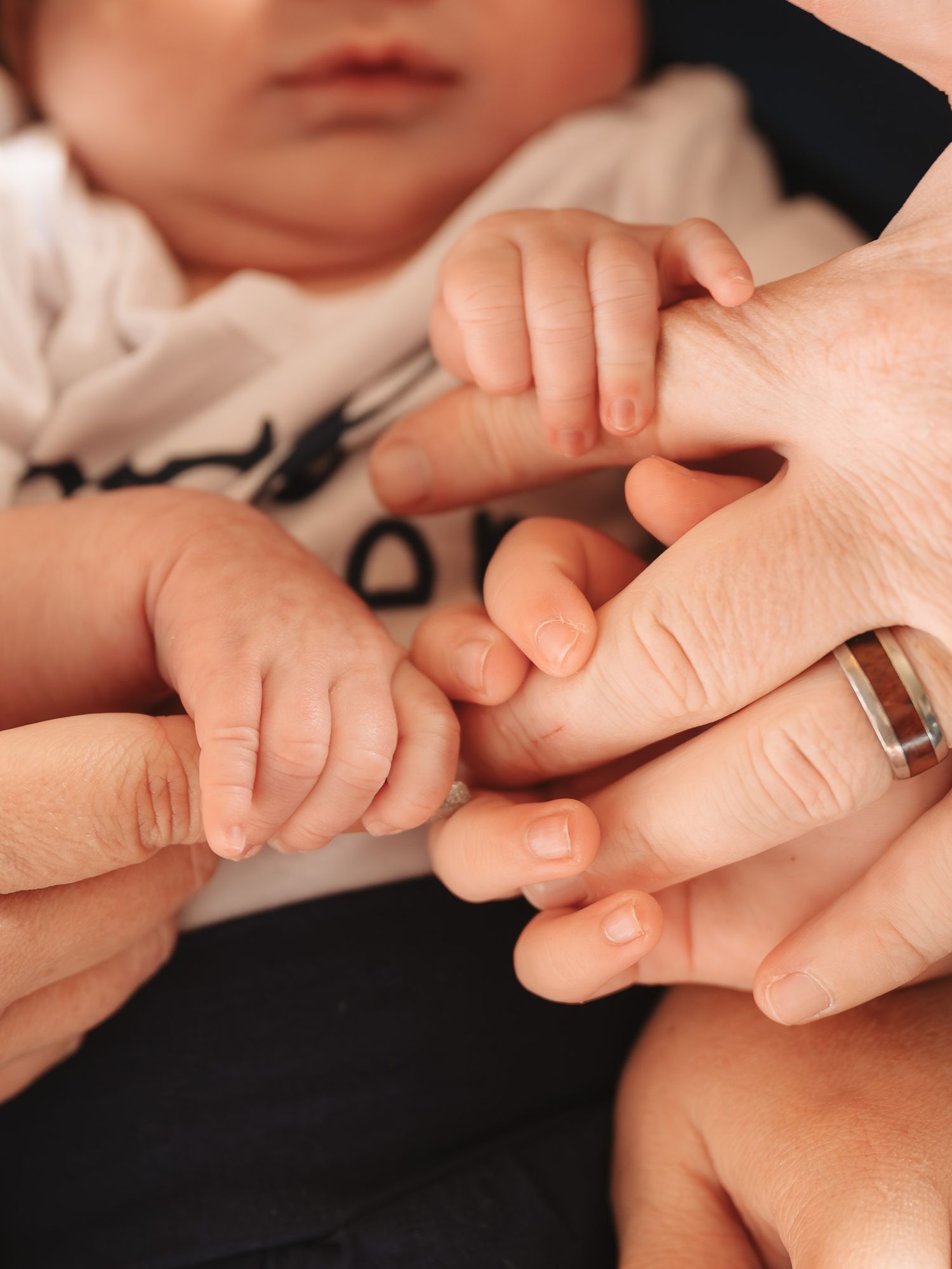Intimate close-up of baby hands holding adult fingers against a dark background.