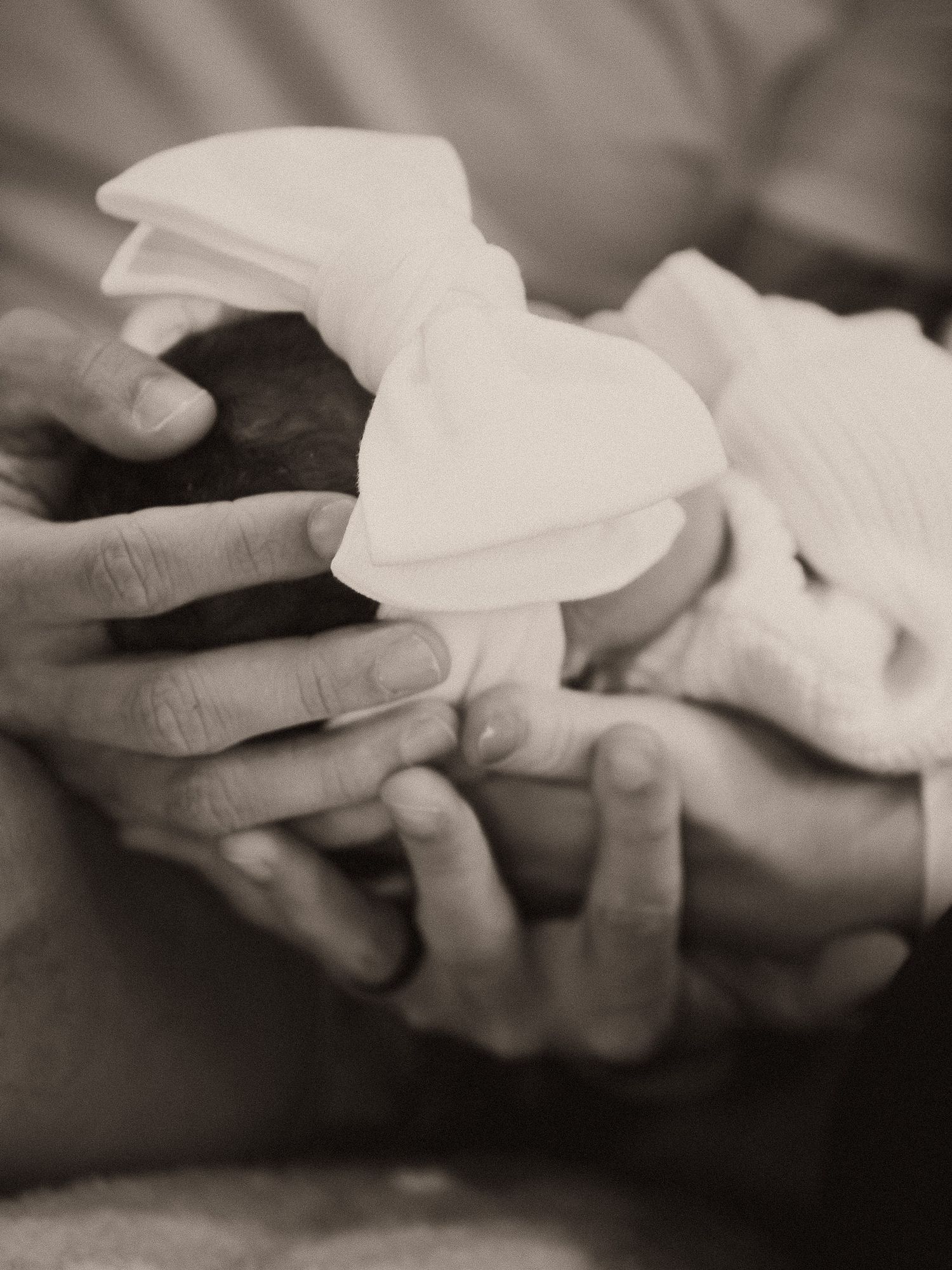 Black and white photo of adult hands cradling a newborn baby girl wearing a white bow headband.