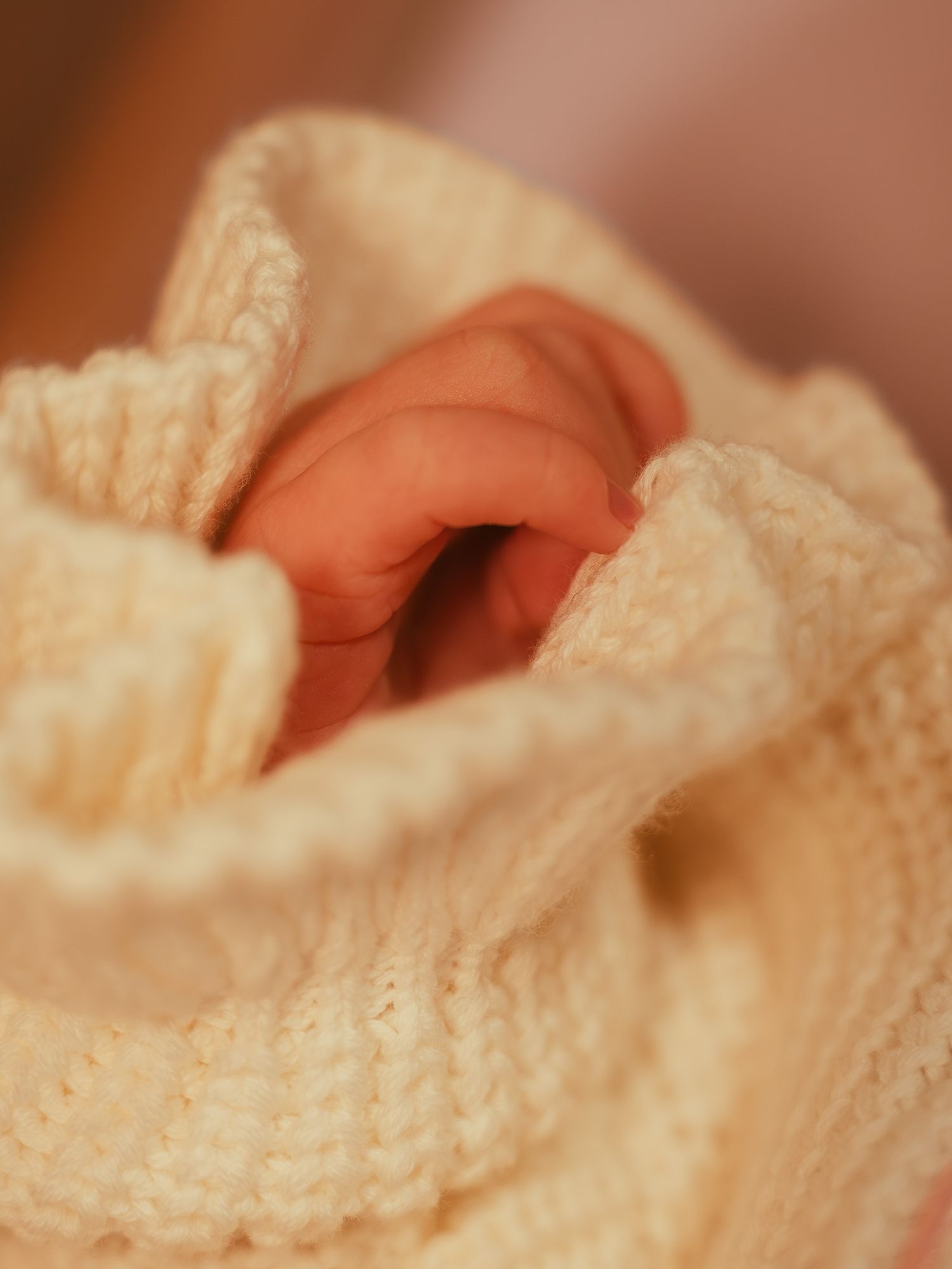 Newborn baby hand wrapped in a soft cream knit blanket, close-up photography.