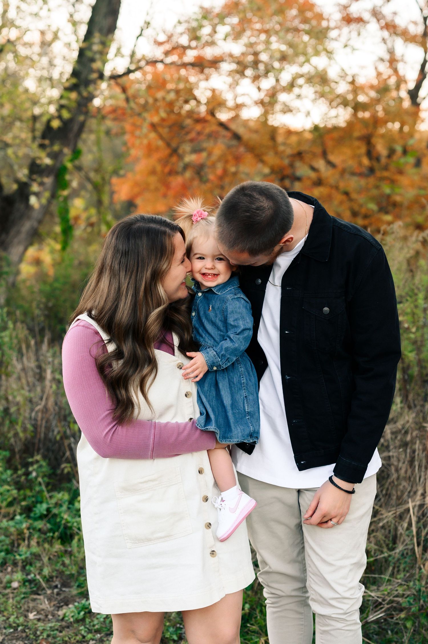 A family shares tender moments in a series of fall photos with autumn foliage in the background.