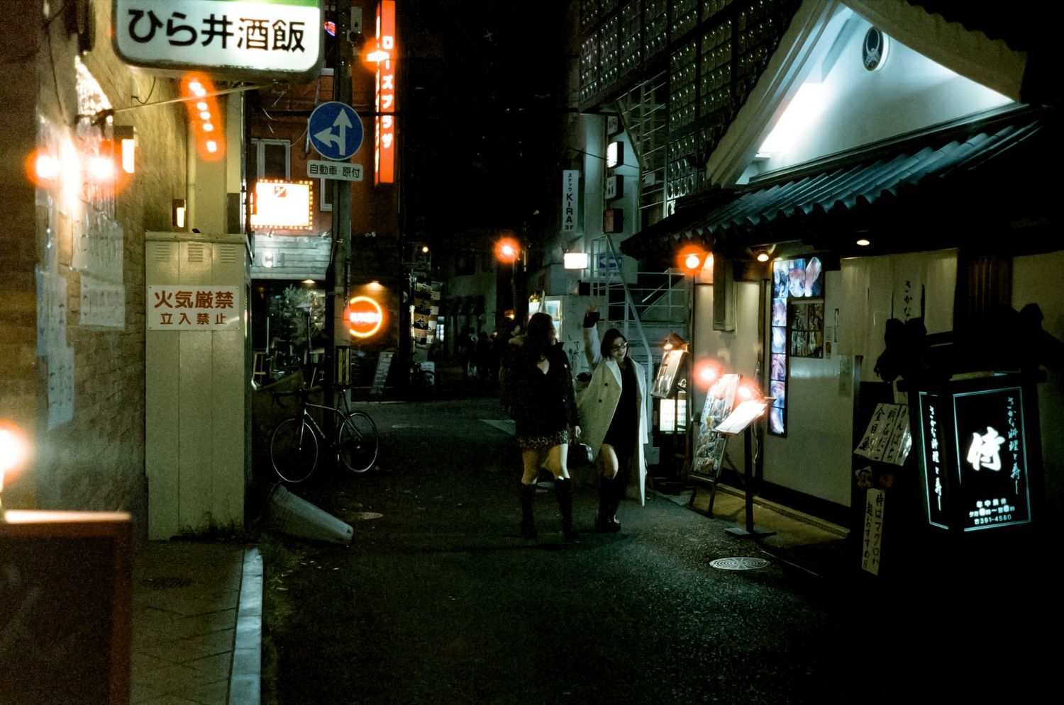 Dimly lit narrow alleyways in Japan at night with glowing signs and street lamps creating an atmospheric urban scene.