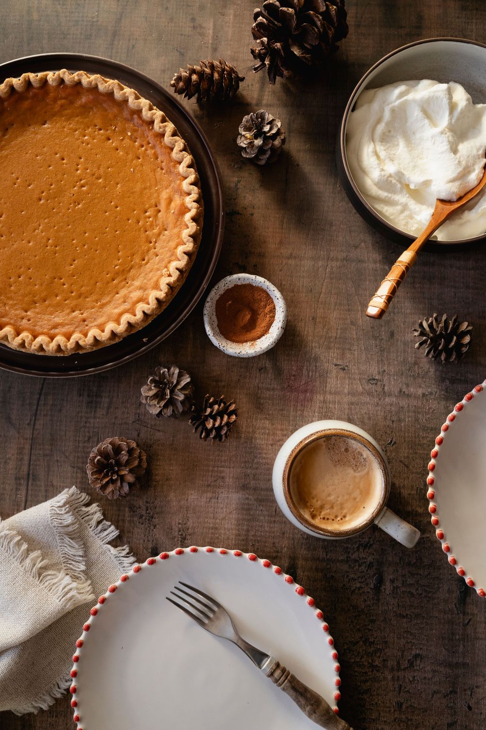 Homemade pumpkin pie with whipped cream and striped straws on dark wooden surface.