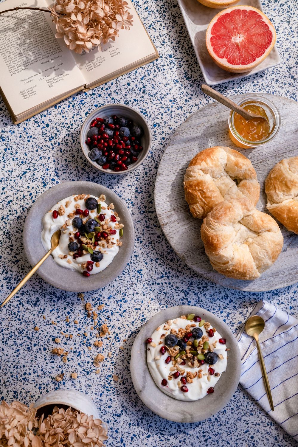 Brunch setting with croissants, yogurt, berries and grapefruit on blue patterned surface.