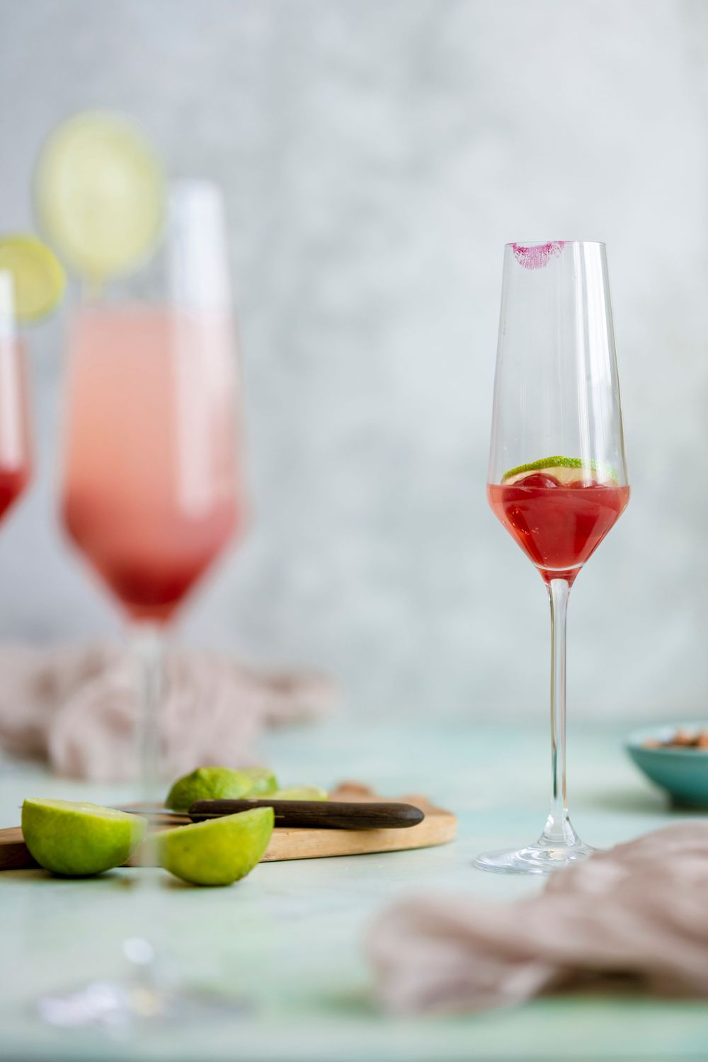 Elegant cocktail glasses with pink drinks and lime garnish on light background.
