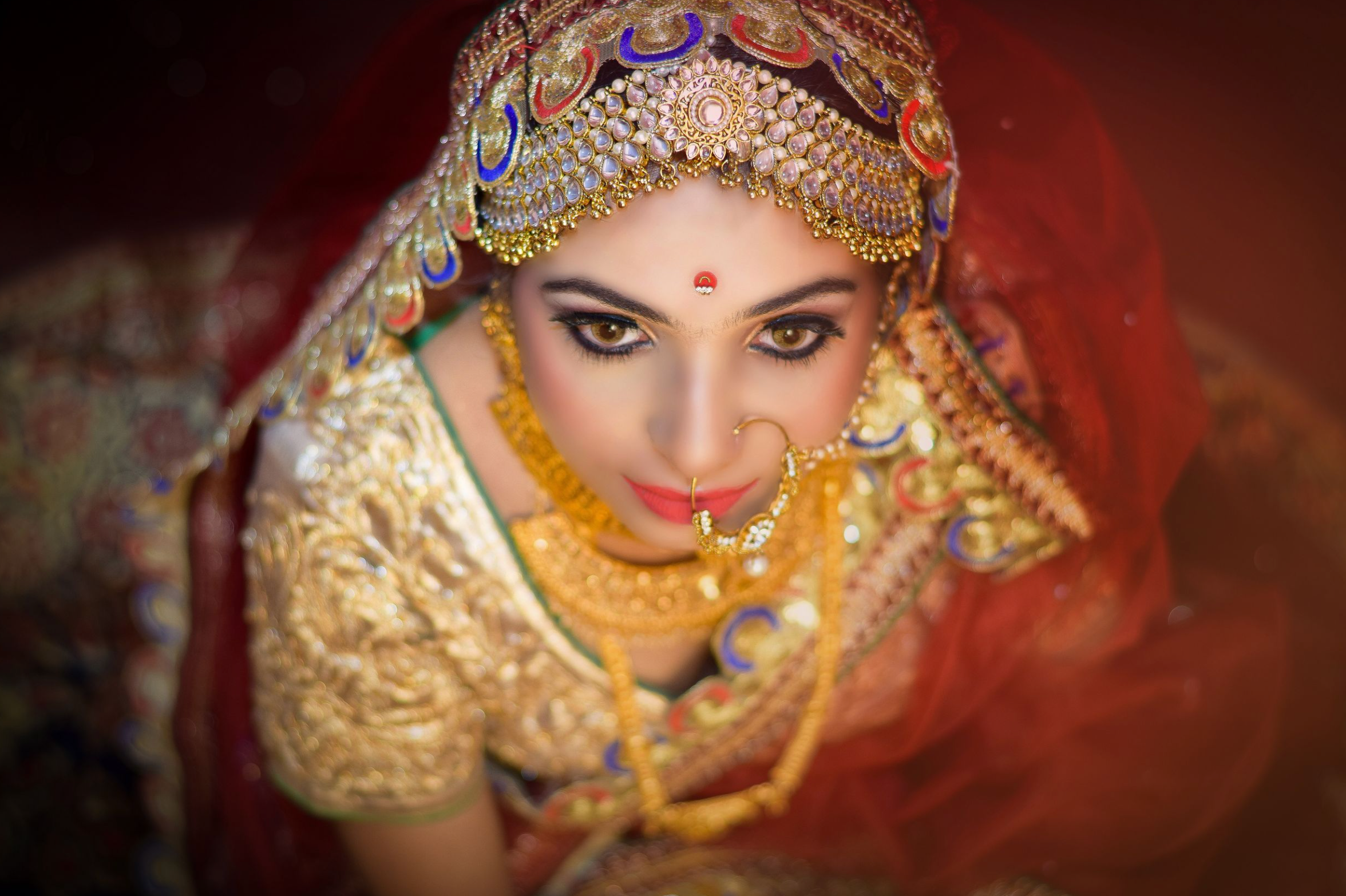 Traditional Indian bride wearing ornate gold jewelry and red attire with intricate details and embellishments.