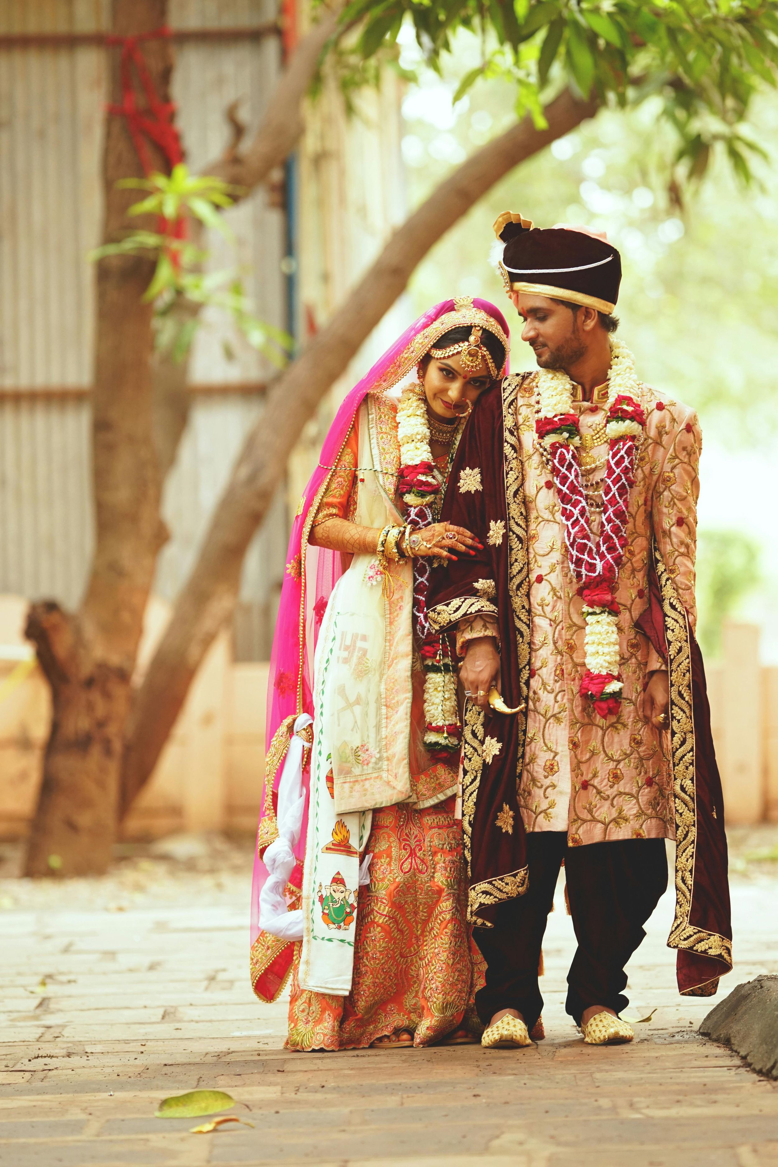 A couple in traditional Indian wedding attire walks together through a tree-lined path during their wedding photoshoot.