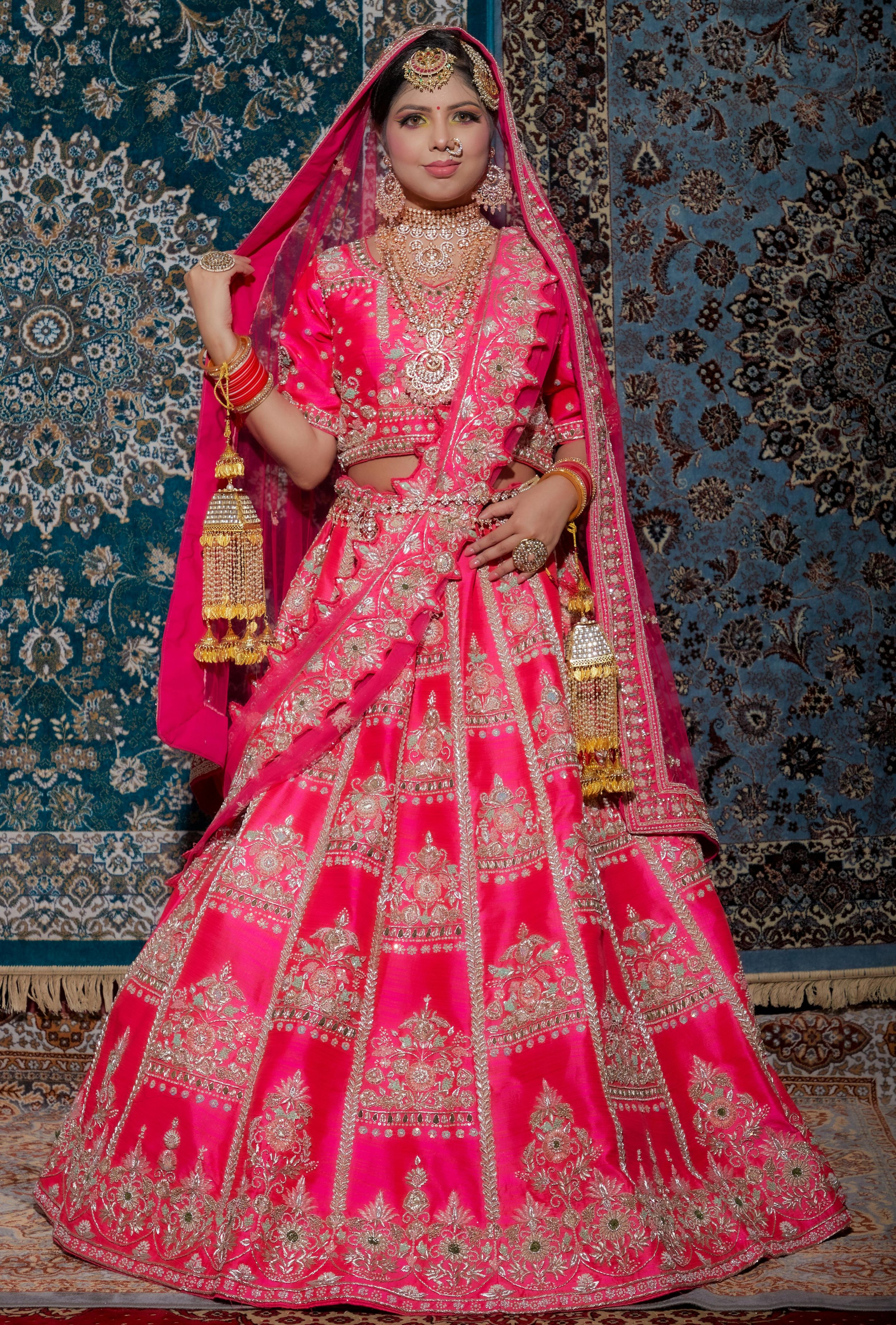 Traditional Indian bridal lehenga in vibrant pink with intricate gold embroidery and matching dupatta against ornate backdrop.