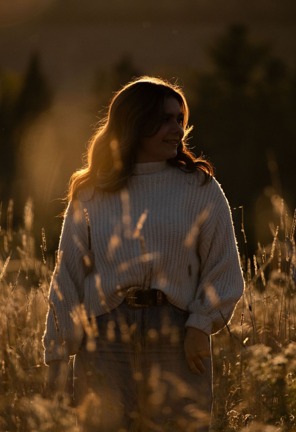 Silhouette of someone in a sweater among tall grass during sunset with warm backlighting.