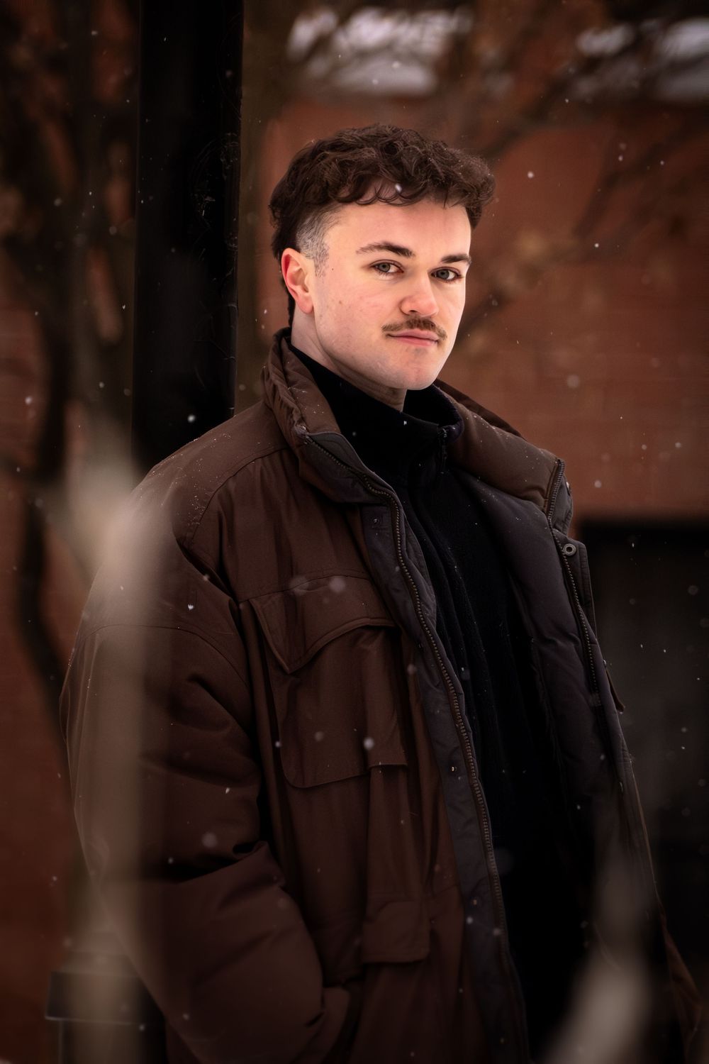 Person wearing a dark winter coat smiles while standing outdoors in snowy winter weather.