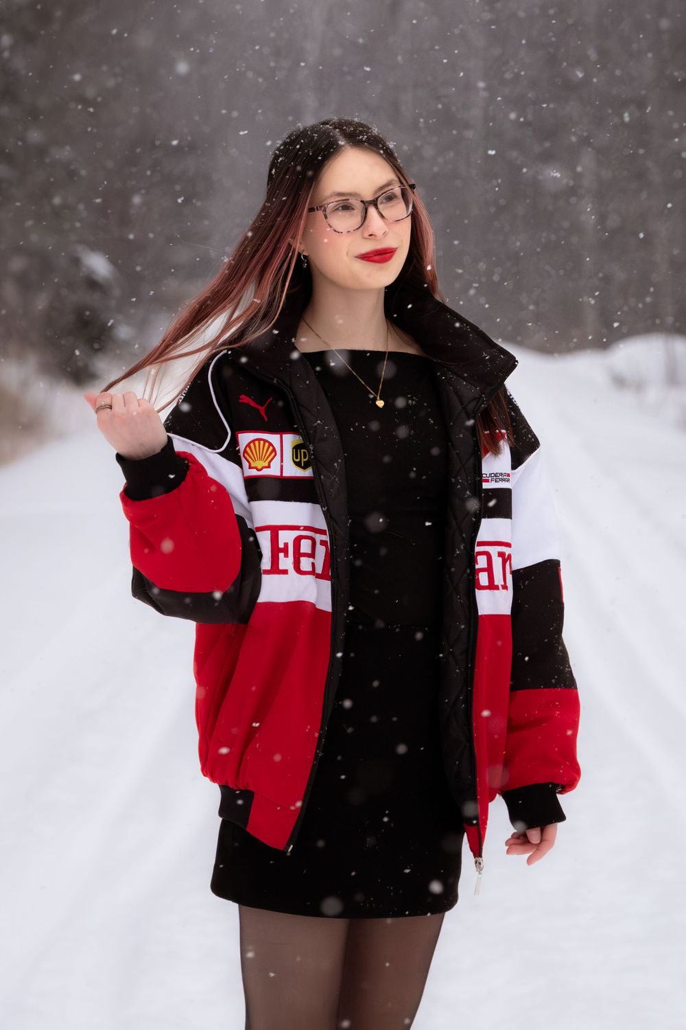 A winter fashion photoshoot in the snow featuring a red and white varsity jacket and black leggings.