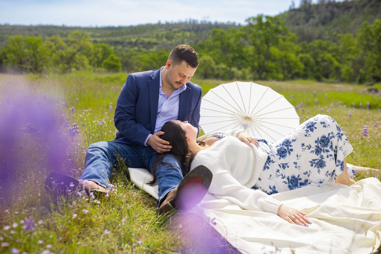 Romantic couple lying in a lavender field with white parasol on sunny day.