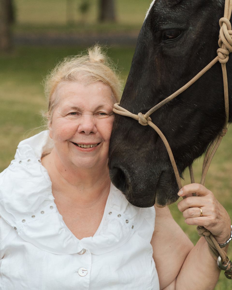 A smiling person poses with a black horse  photos outdoors during a family photoshoot with a horse in sydney rouse hill
