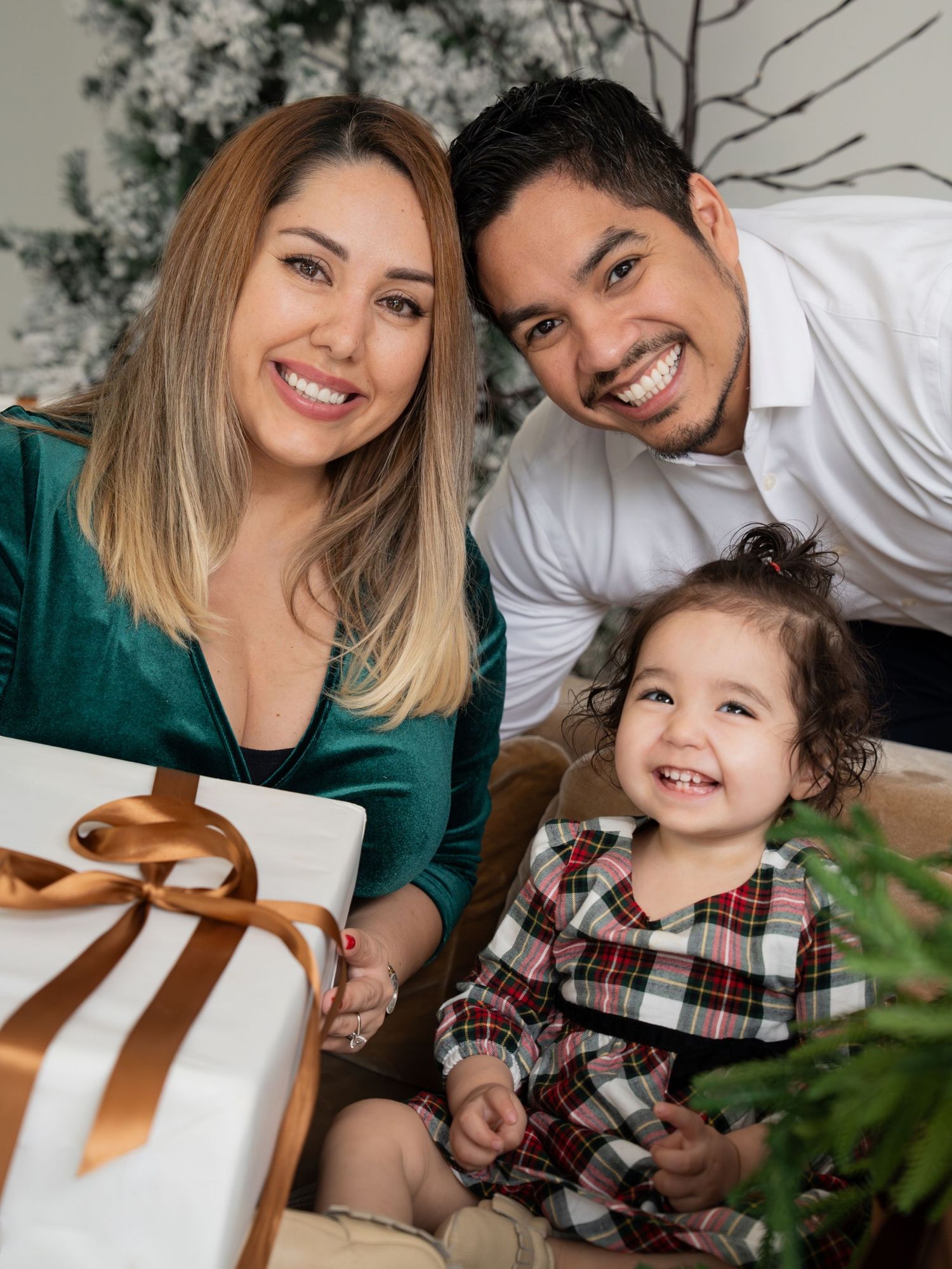 A family poses together for holiday photos with wrapped presents and Christmas decorations in the background.