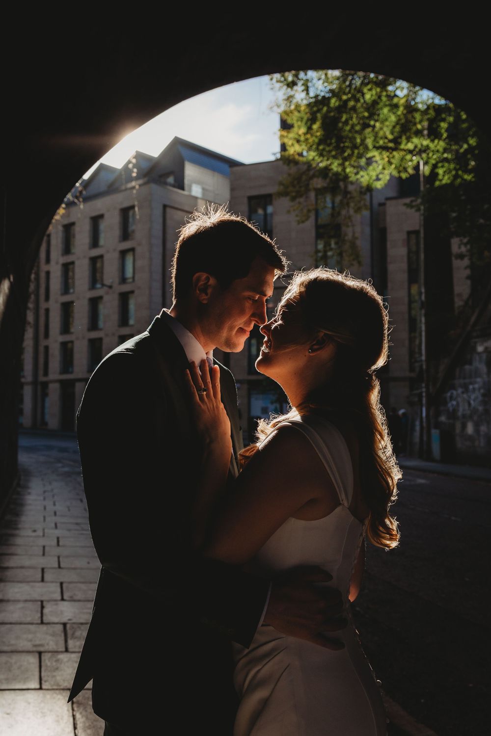 A romantic silhouetted couple shares an intimate moment against a backlit urban backdrop.
