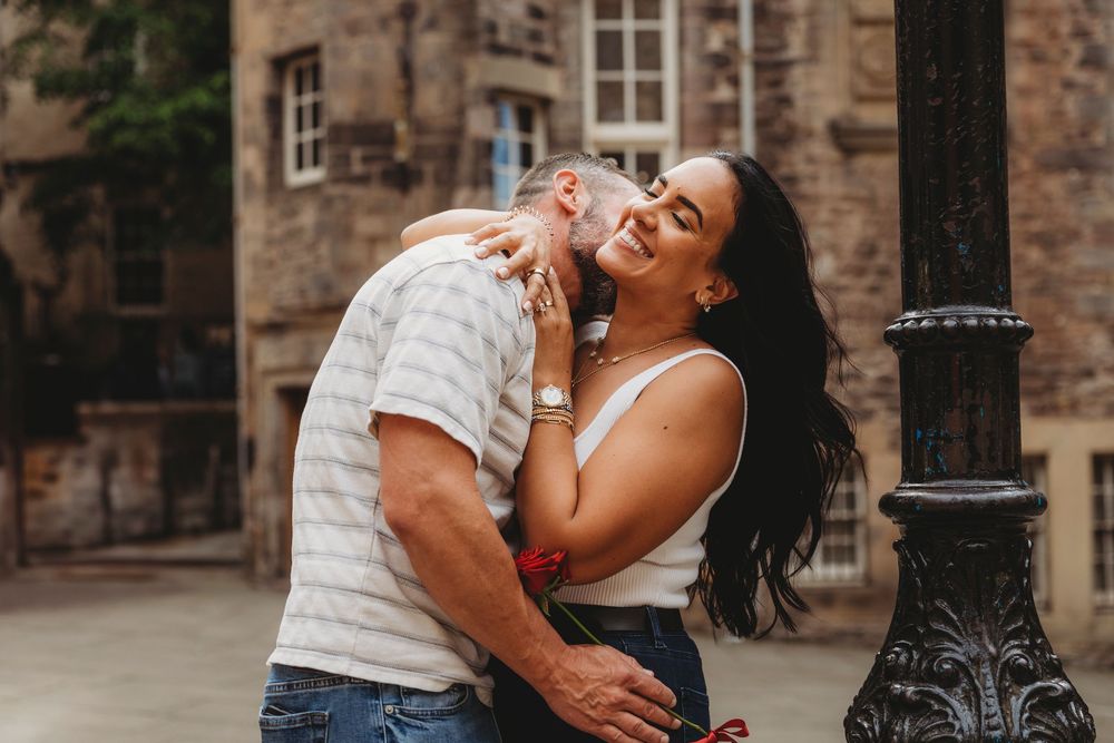 Couple sharing a romantic moment together while laughing and embracing against a stone building exterior.