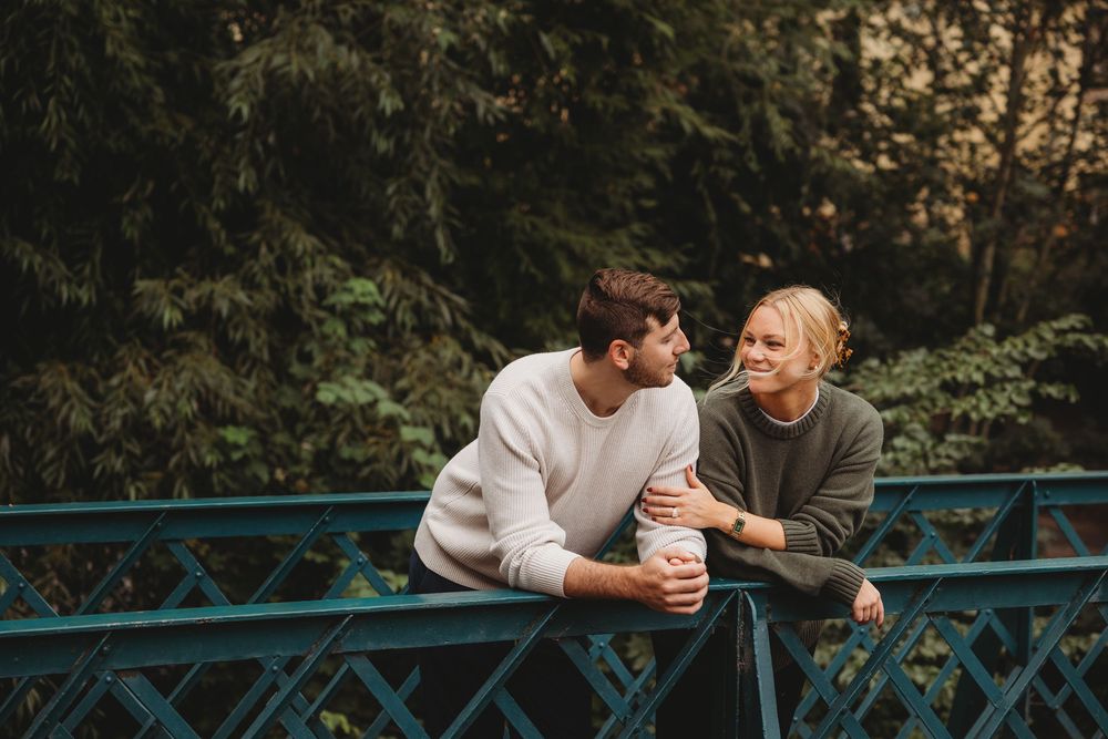 Couple sharing a romantic moment on turquoise bridge railing while holding coffee cups at sunset.