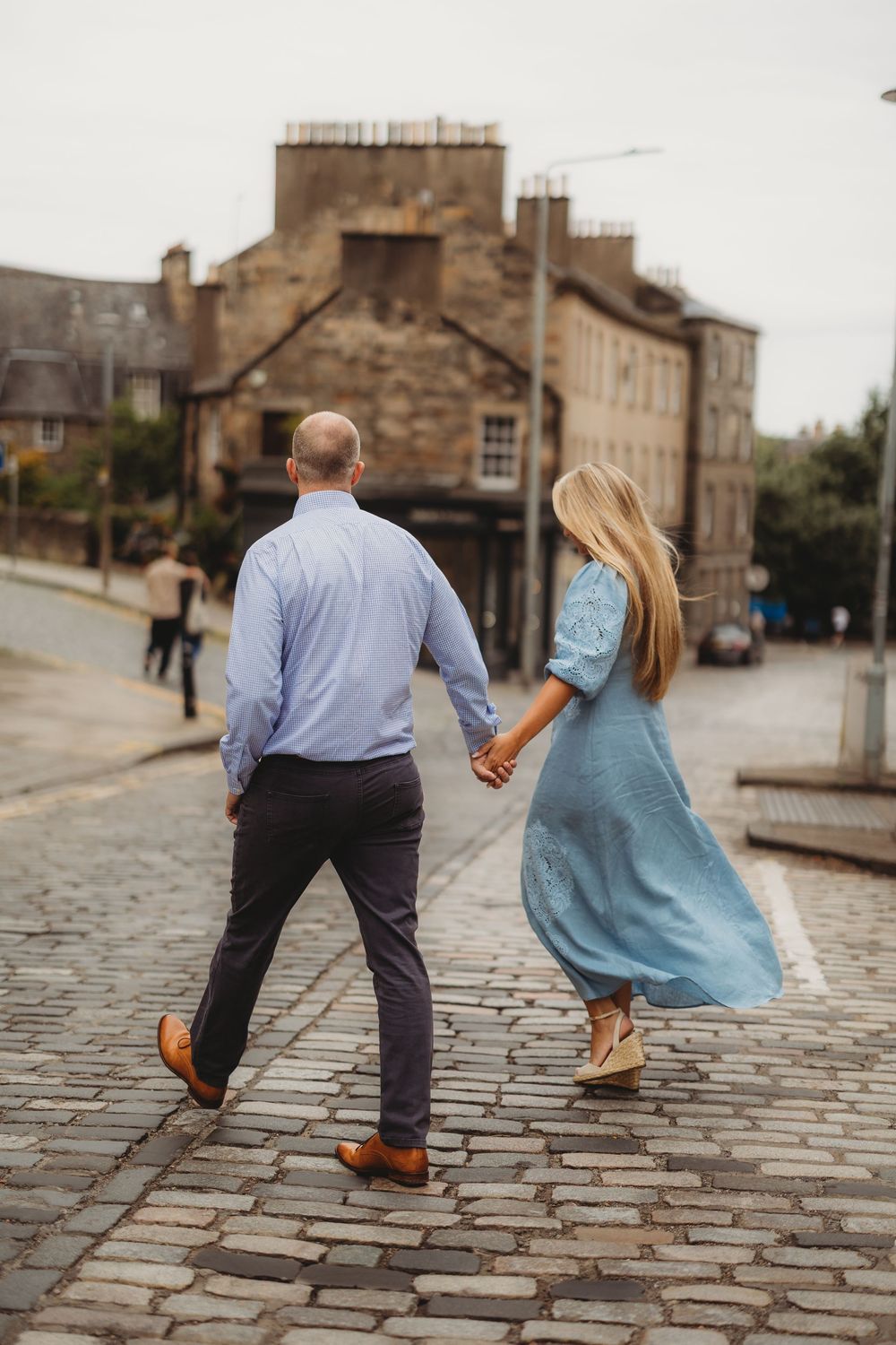 Couple walking together on cobblestone street holding hands in Edinburgh's historic district.
