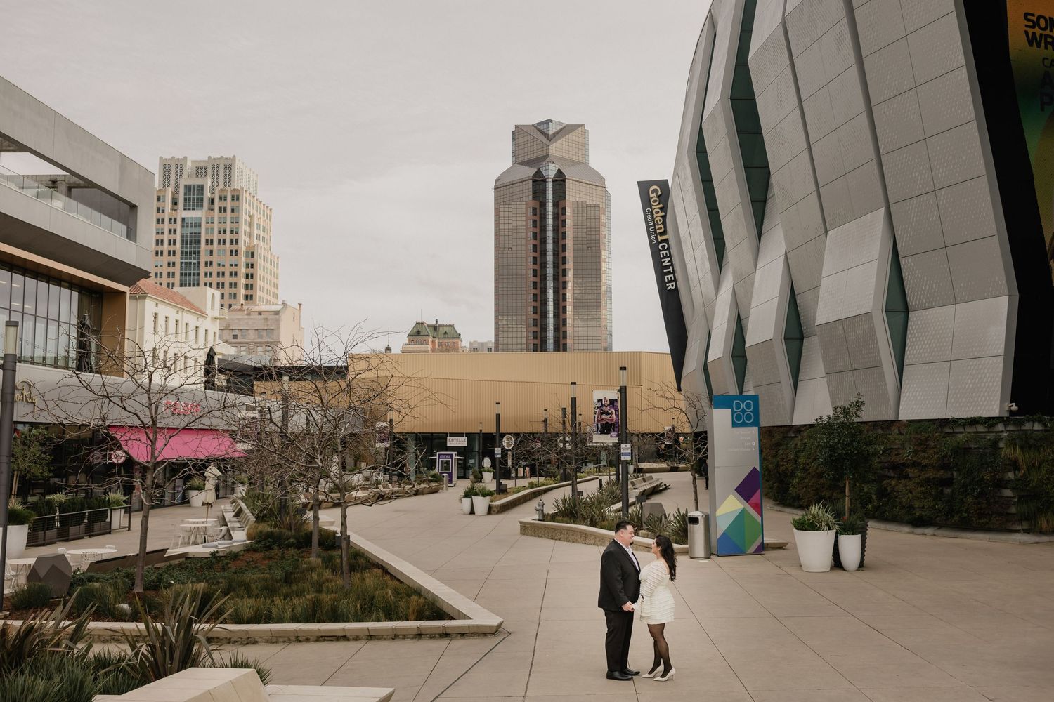 Couple sharing a romantic moment in an urban plaza surrounded by modern architecture and city skyscrapers.