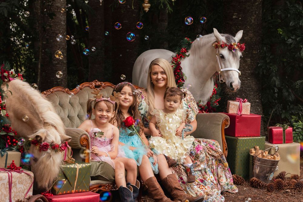 Magical outdoor photo session with bubbles, red flowers, and a white pony against a dark forest backdrop.