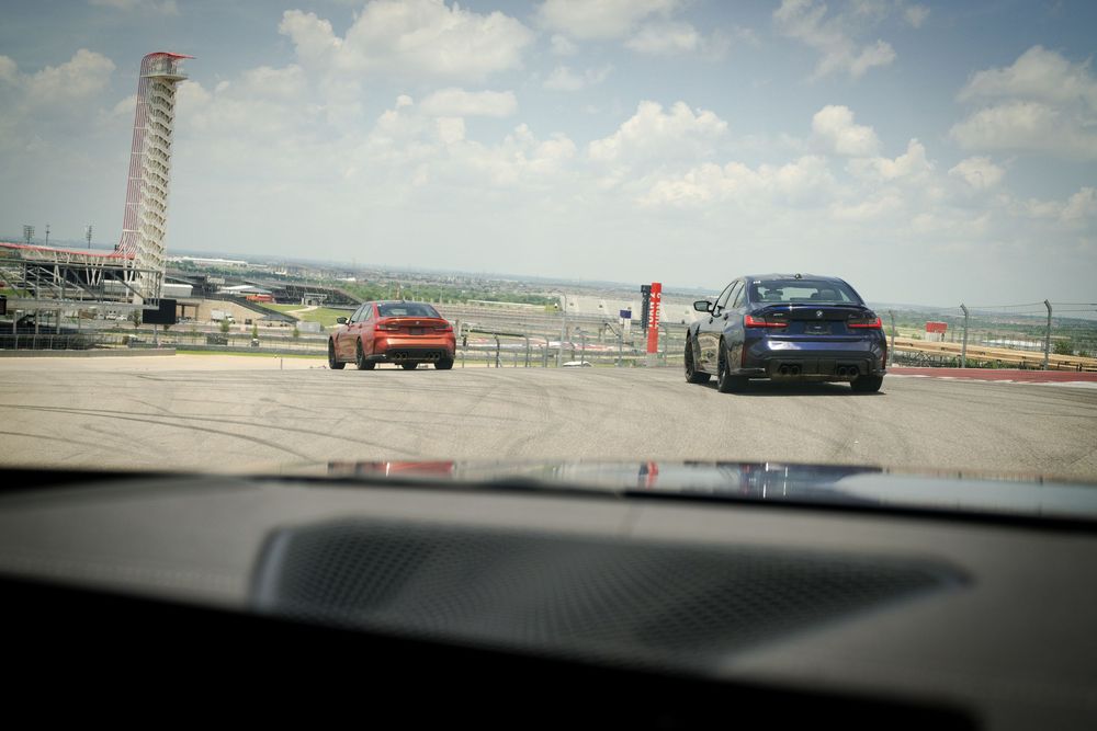 View through windshield of cars on a race track with pit lane visible.
