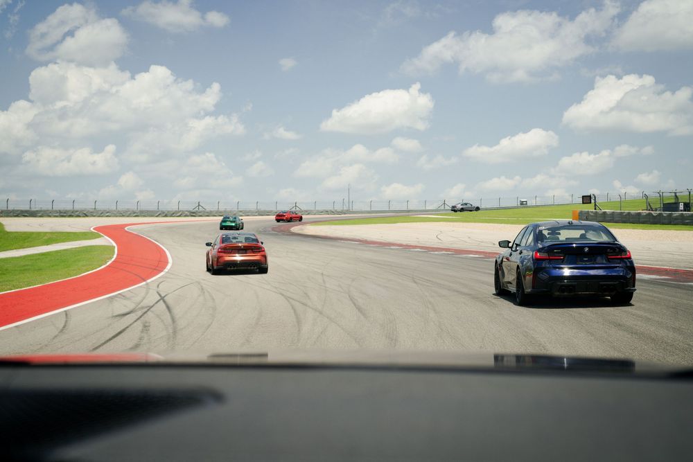 Sports cars driving on a race track with red and white curbing.