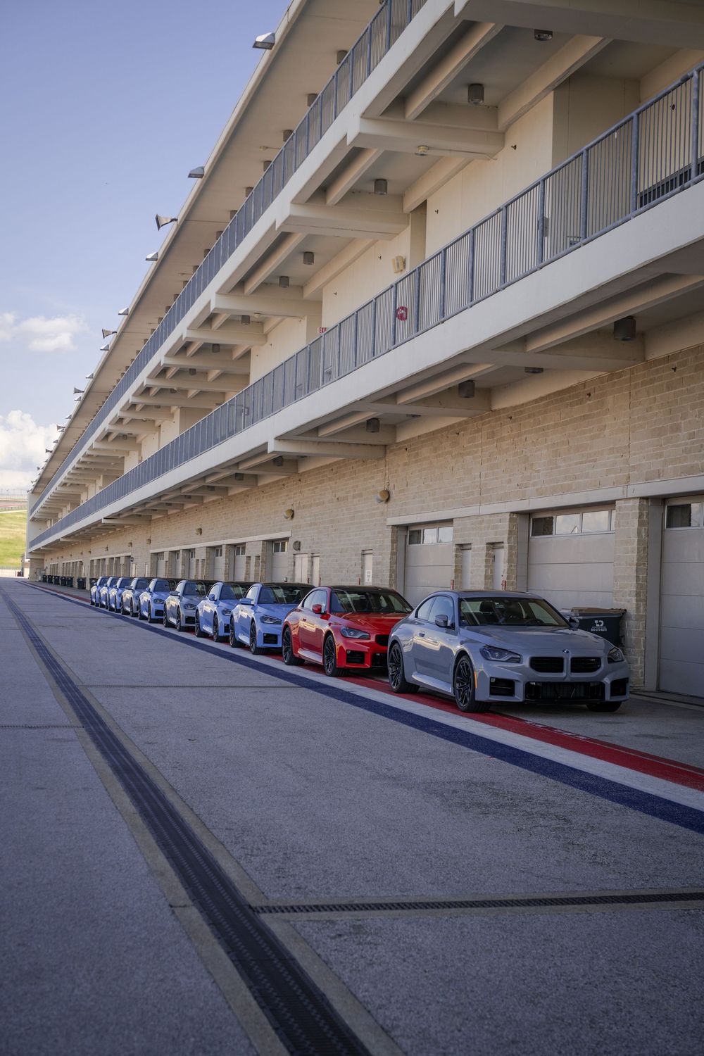 Line of colorful BMW vehicles parked in covered pit lane garages.